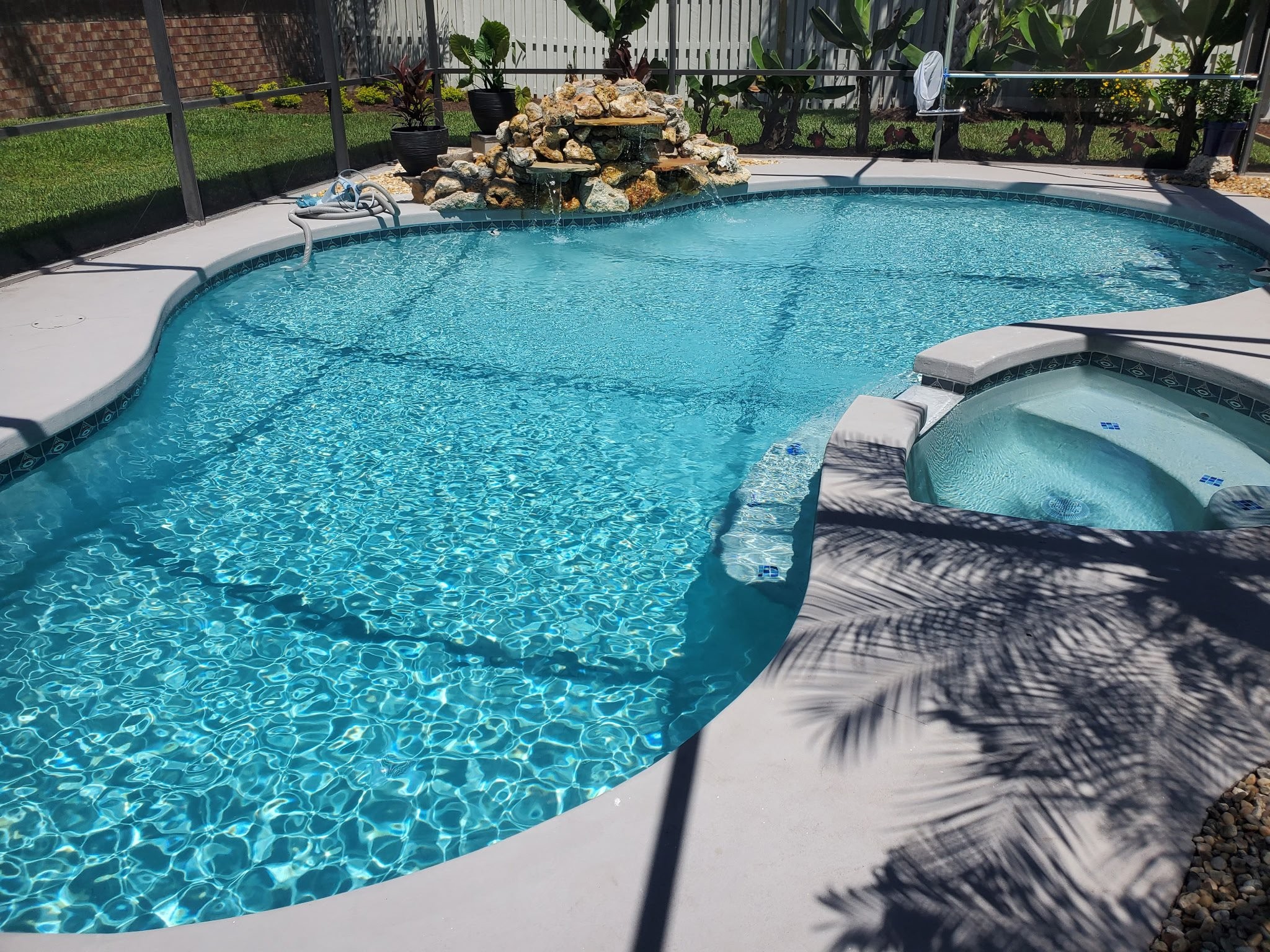 Crystal-clear residential pool with rock waterfall, spa, and tropical landscaping