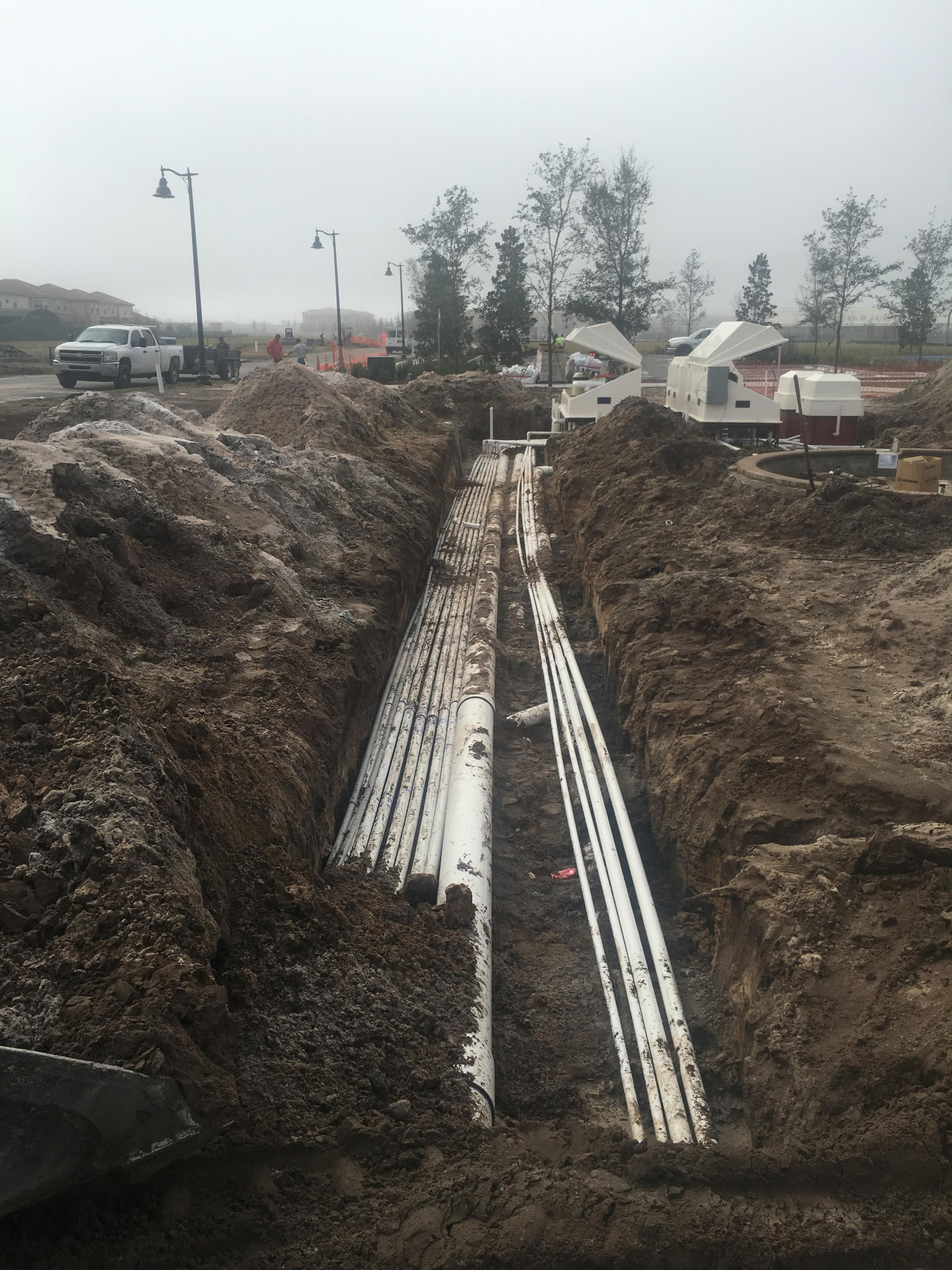 Underground plumbing trench with white PVC pipes running to commercial pool equipment pad